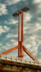 A Rákóczi híd narancsvörös pilonjának alsó nézetű, részletgazdag fotója a drámai, felhős égbolt előtt.